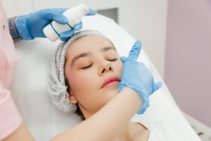 Beautician's hands apply cream on woman's forehead. Skin treatment. Spa beauty treatments.